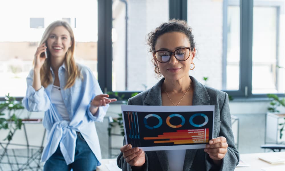 African american businesswoman holding document with NPS results while colleague talking on smartphone in the background